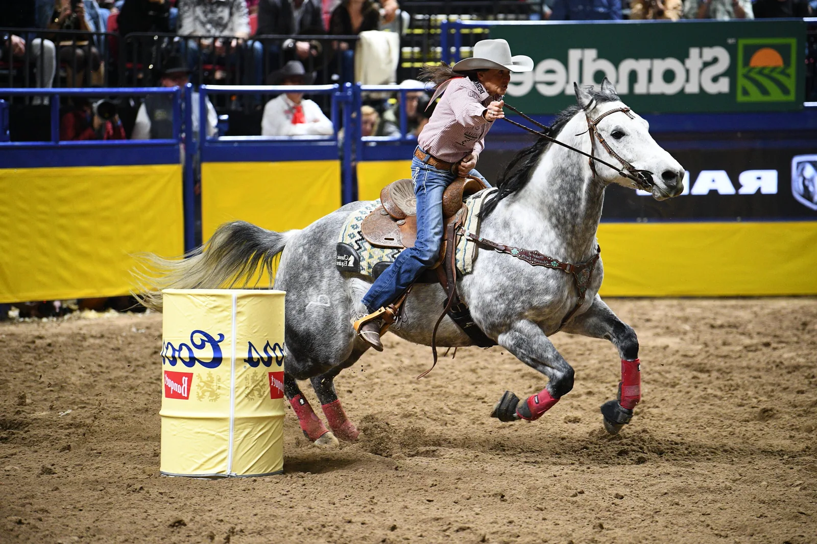A barrel racer and horse rounding a barrel in an arena.