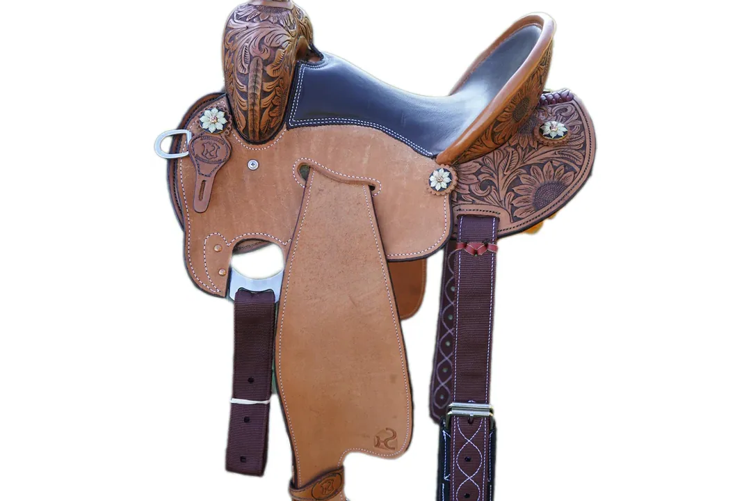 A barrel racer adjusting a saddle on a horse in a stable.