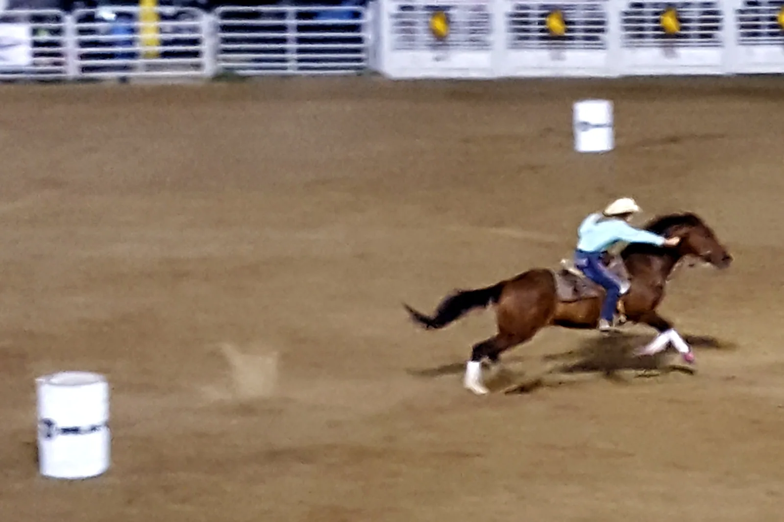 A barrel racer and horse making a wide turn around a barrel in an arena.
