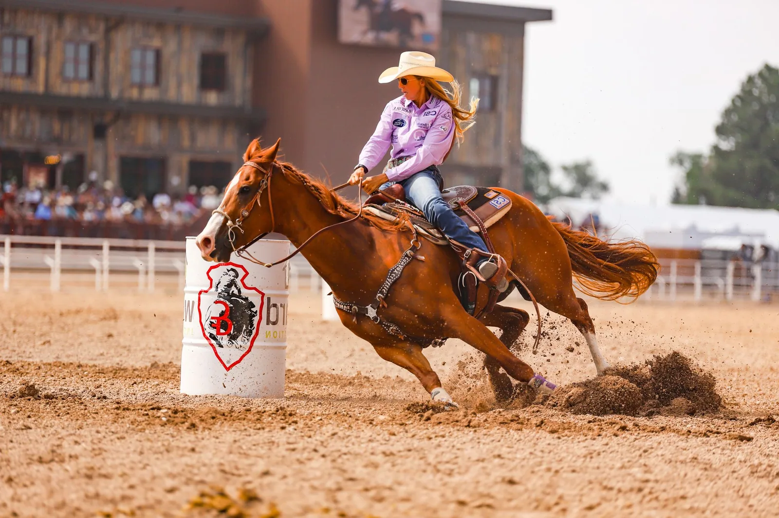 A horse and rider racing around a barrel, muscles straining, dust flying.
