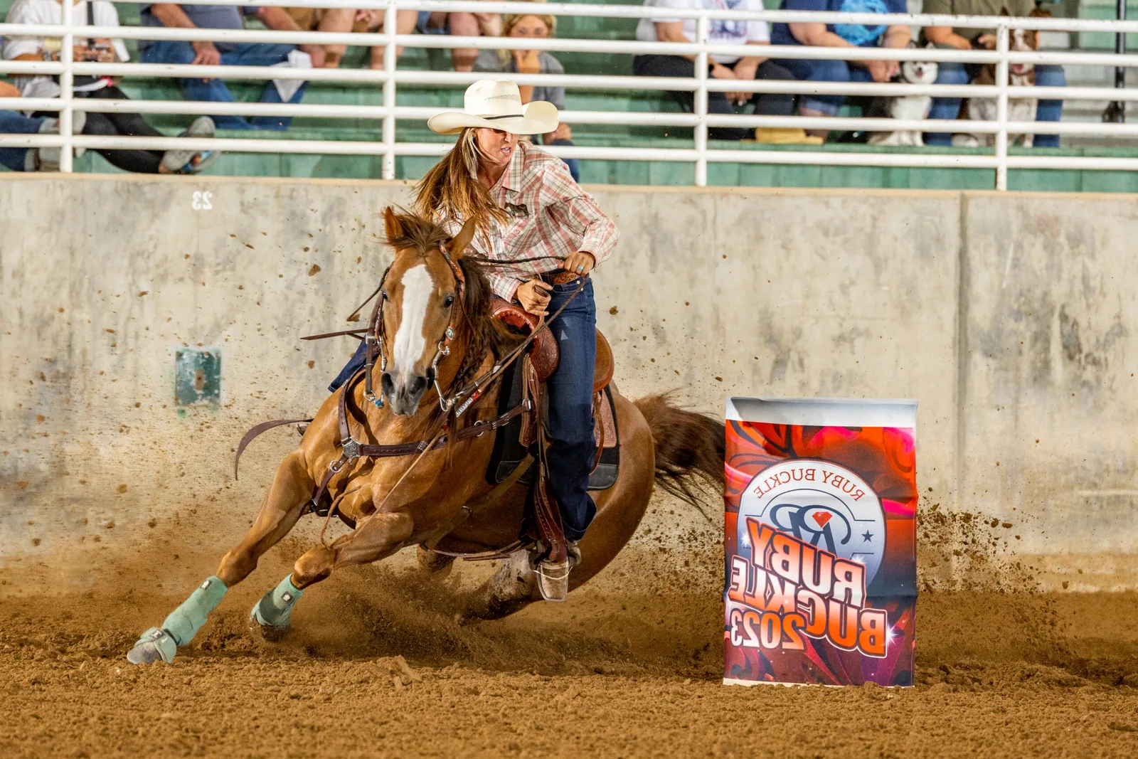 A barrel racer and horse speeding around a barrel in an arena.